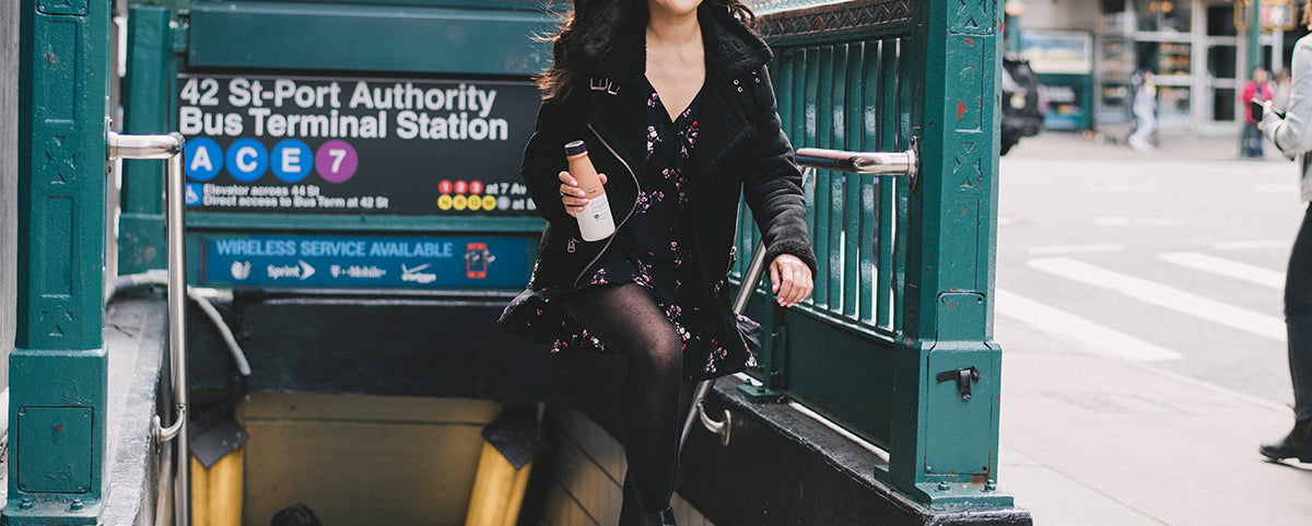 Woman walking out of the subway with a Soylent drink in hand